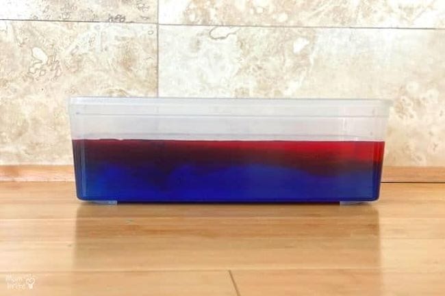 Plastic bin of colored water, with red on top and blue on the bottom