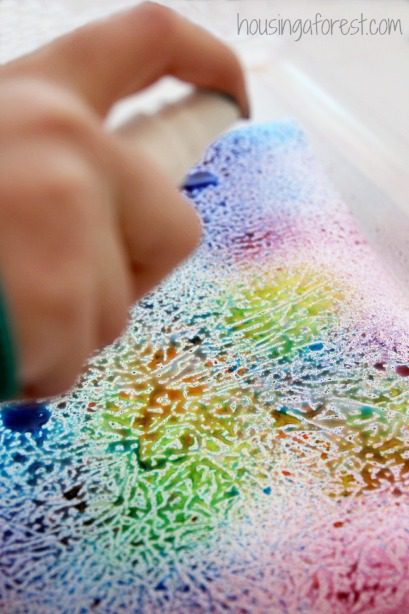 A child's hand is shown in front of a bright colored wax paper drawing.
