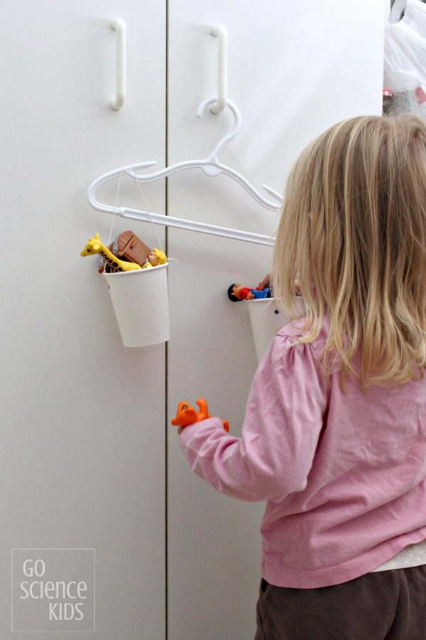 A little girl is seen filling a cup in a homemade scale. 